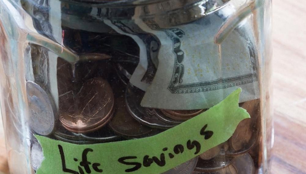 A glass jar labelled Life Savings filled with coins and notes, representing long-term wealth building for UAE residents