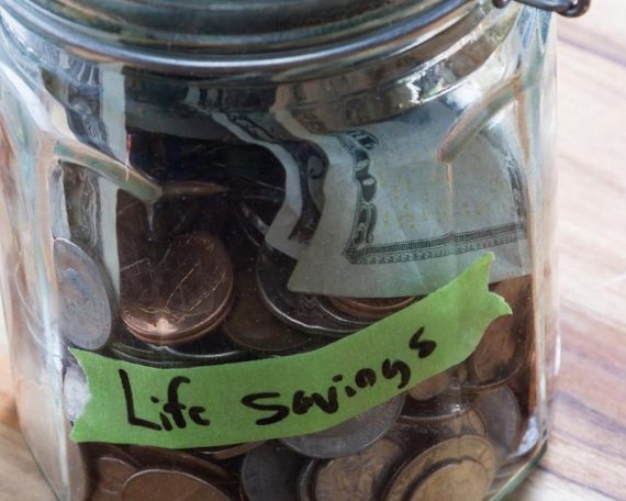 A glass jar labelled Life Savings filled with coins and notes, representing long-term wealth building for UAE residents